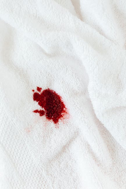 A close-up of a white textured fabric surface, likely a bedsheet or upholstery material, with a prominent red stain in the center, indicating a spill or stain requiring surface cleaning. The fabric appears clean apart from the stain, with a soft sheen under neutral lighting. The image highlights the need for deep cleaning or stain removal to restore hygiene and appearance, consistent with home or commercial cleaning practices that Carpet Cleaning Maida Vale offers in their specialist domestic cleaning services.